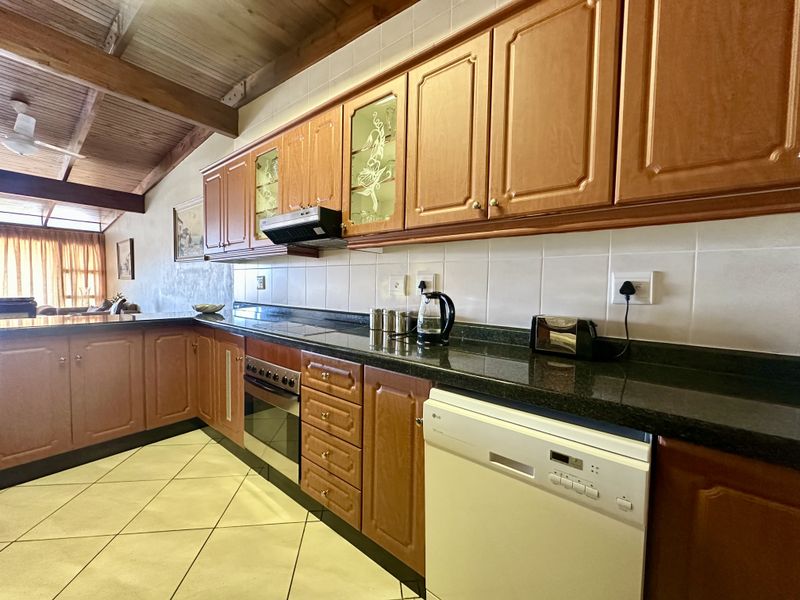 A functional kitchen featuring timber cabinetry, granite countertops, tiled backsplash, and exposed timber ceiling beams, offering a warm and traditional aesthetic.