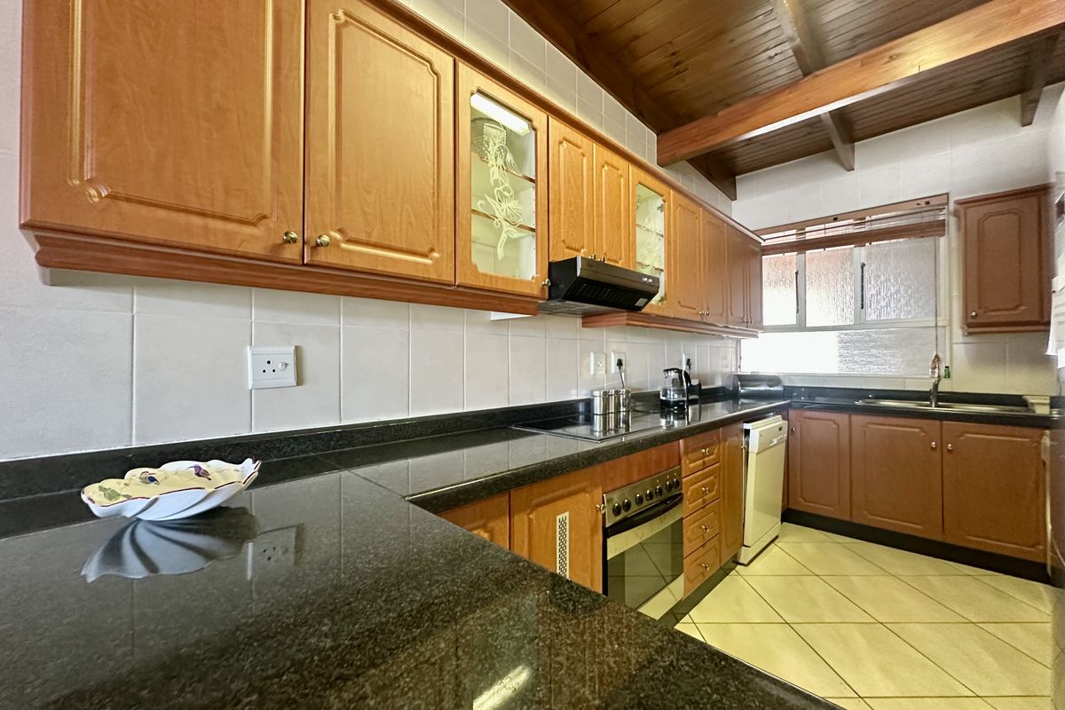 A functional kitchen featuring granite countertops, wooden cabinetry, built-in oven, extractor fan, and exposed timber ceiling beams with tiled flooring.