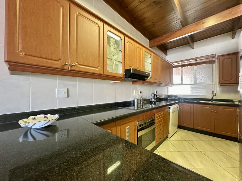 A functional kitchen featuring granite countertops, wooden cabinetry, built-in oven, extractor fan, and exposed timber ceiling beams with tiled flooring.