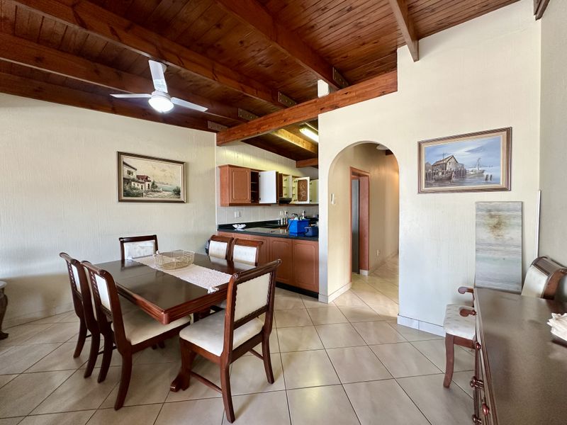 Open plan living and dining area featuring exposed timber beam ceilings, tiled flooring, and an adjoining kitchen with granite countertops and wooden cabinetry.