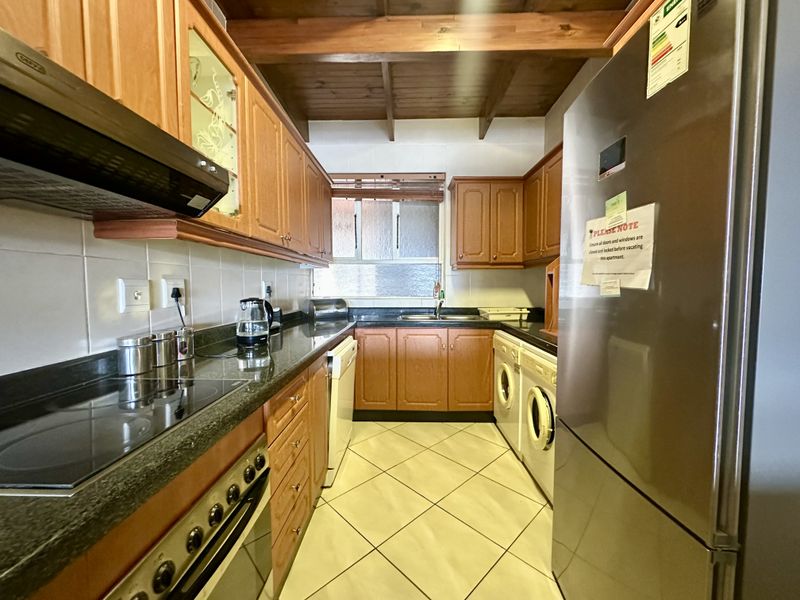 A functional kitchen featuring wooden cabinetry, granite countertops, built-in appliances, and exposed timber ceiling beams, offering a warm and practical workspace.
