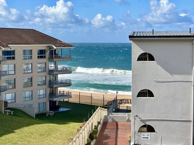 A scenic view of the ocean and beach framed by apartment buildings, showcasing the coastal location and exterior building architecture.
