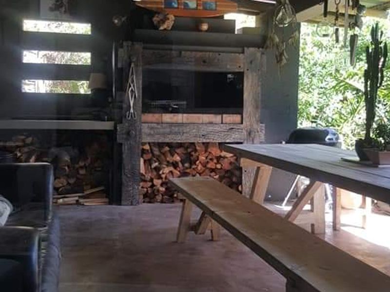 Covered outdoor patio featuring a rustic built-in braai, exposed timber rafters, corrugated metal roofing, and concrete flooring, ideal for outdoor entertaining.