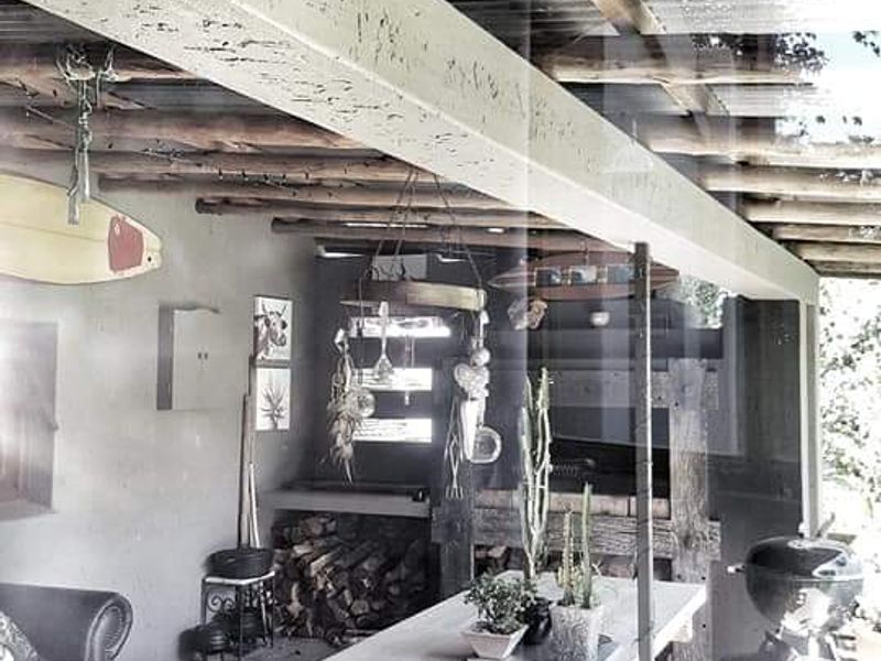 A rustic covered patio area featuring exposed timber rafters, a corrugated metal roof, and a built-in fireplace, ideal for outdoor entertaining.