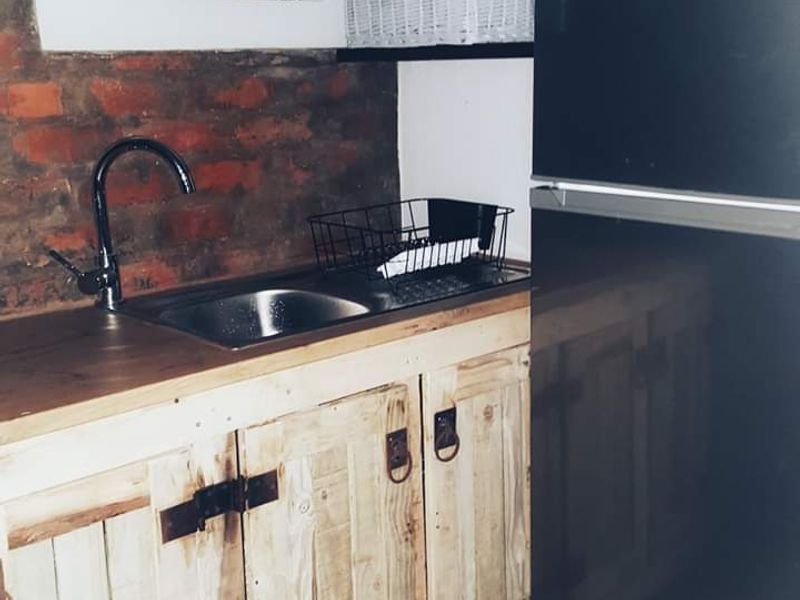 A rustic kitchen area featuring exposed brick walls, custom timber cabinetry, a stainless steel sink with a modern faucet, and tiled flooring.