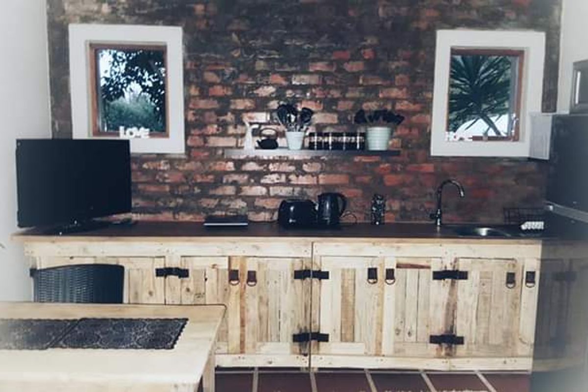 A rustic kitchen area featuring exposed brick walls, custom timber cabinetry, and a wooden countertop with an integrated sink.