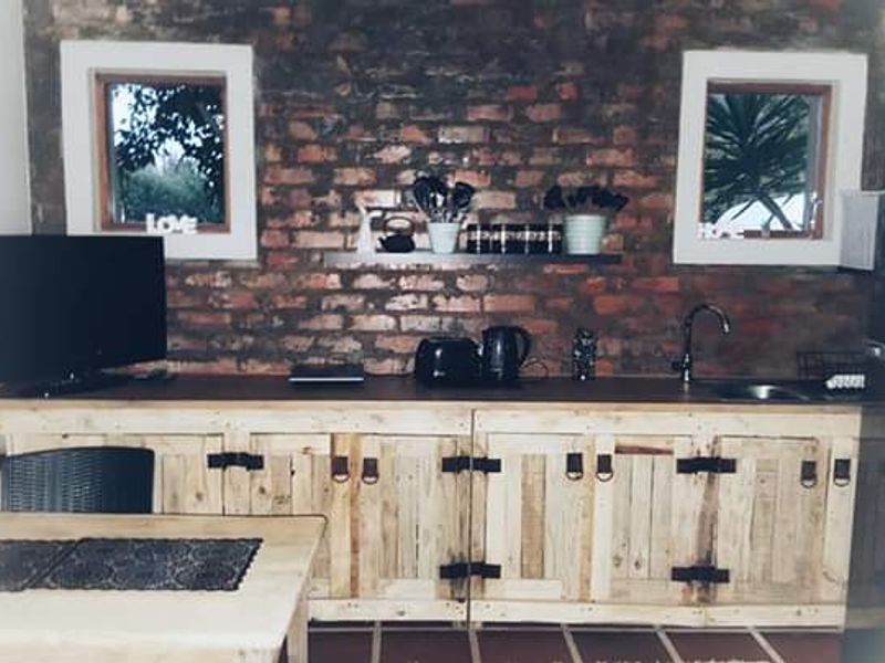 A rustic kitchen area featuring exposed brick walls, custom timber cabinetry, and a wooden countertop with an integrated sink.