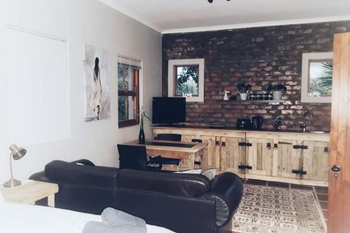 Open plan living area featuring an exposed brick wall, rustic wooden cabinetry, and integrated kitchen sink, creating a cozy cottage atmosphere.