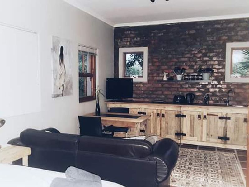 Open plan living area featuring an exposed brick wall, rustic wooden cabinetry, and integrated kitchen sink, creating a cozy cottage atmosphere.