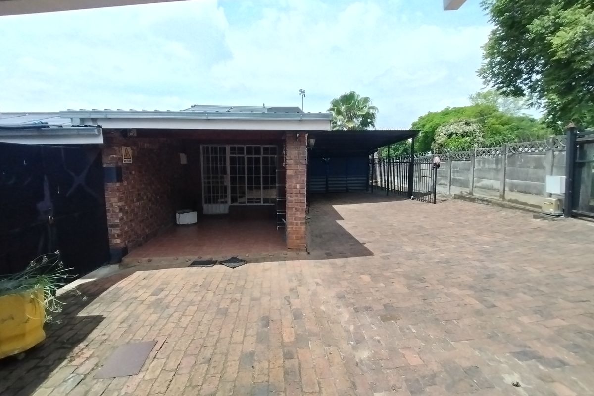 A rear exterior view featuring a paved driveway, covered patio area, and secure perimeter walling.