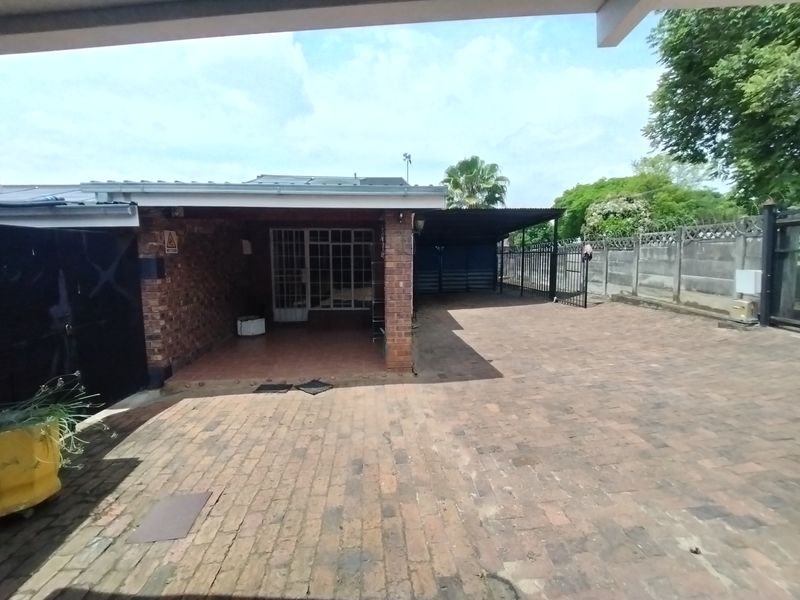 A rear exterior view featuring a paved driveway, covered patio area, and secure perimeter walling.