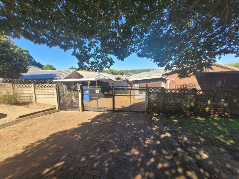 Front view of the property featuring a paved driveway, secure metal gate, and perimeter walling with security fencing.