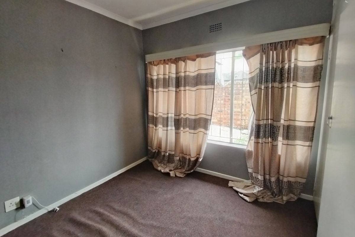 An empty bedroom featuring grey walls, carpeted flooring, and a window fitted with security bars.