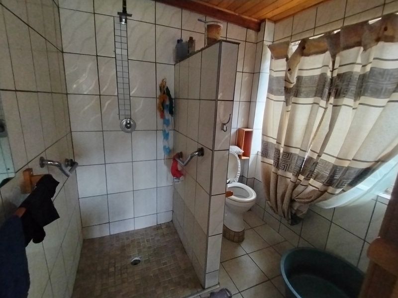 A functional bathroom featuring a tiled shower enclosure, toilet, and timber ceiling, offering a dated aesthetic ready for modernization.