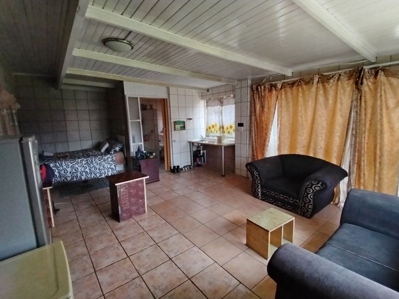 Open-plan living area featuring tiled flooring, exposed beam ceiling, and a small kitchenette area with sink.
