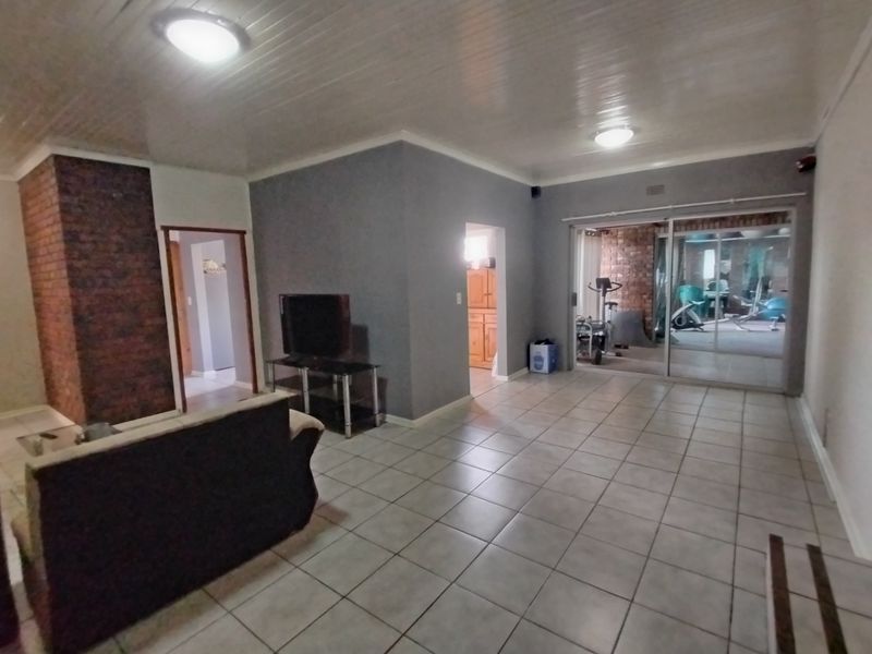 Spacious living room featuring tiled flooring, an exposed brick fireplace, and a sliding glass door leading to an enclosed patio area.