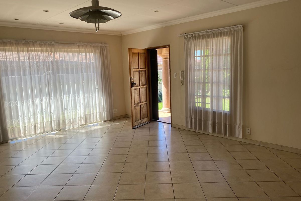 Spacious, light-filled living area featuring neutral tiled flooring, recessed ceiling lighting, and direct access to the exterior through a solid timber entrance door.