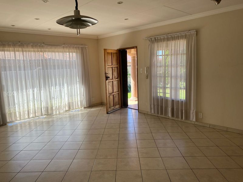 Spacious, light-filled living area featuring neutral tiled flooring, recessed ceiling lighting, and direct access to the exterior through a solid timber entrance door.