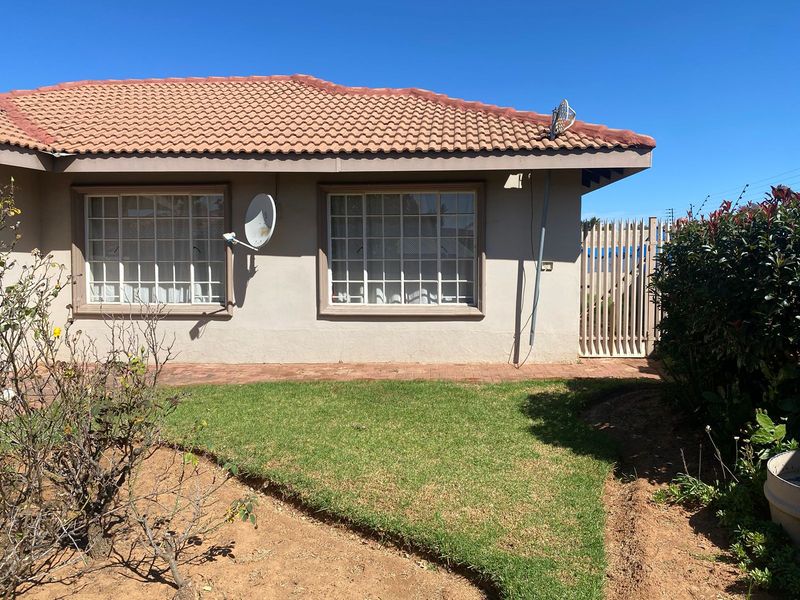 Rear exterior view of the house featuring a tiled roof, brick paved walkway, and a small garden area with a security gate.
