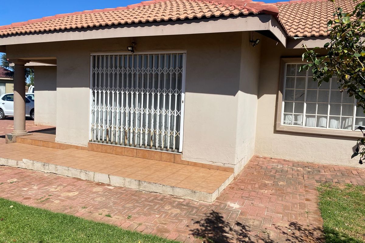 Rear exterior view of the house featuring a tiled patio, brick paved area, and a security gate over the entrance.