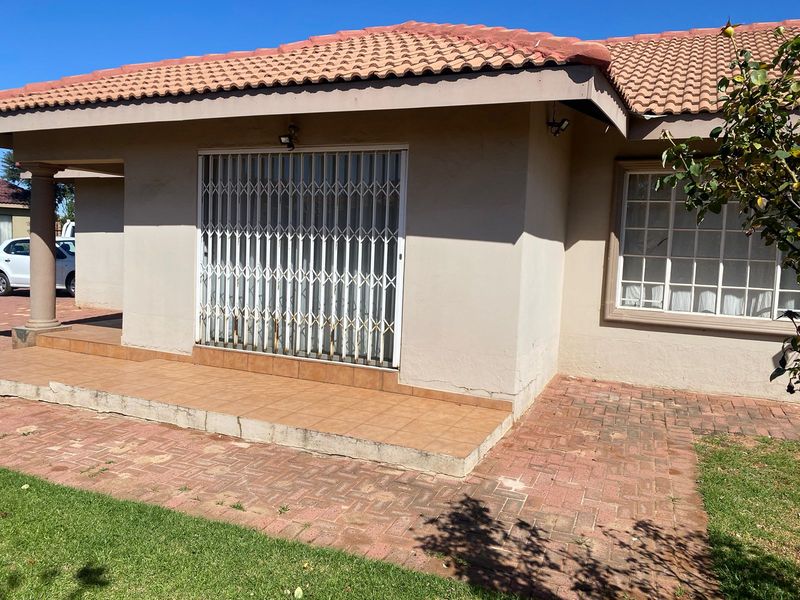 Rear exterior view of the house featuring a tiled patio, brick paved area, and a security gate over the entrance.