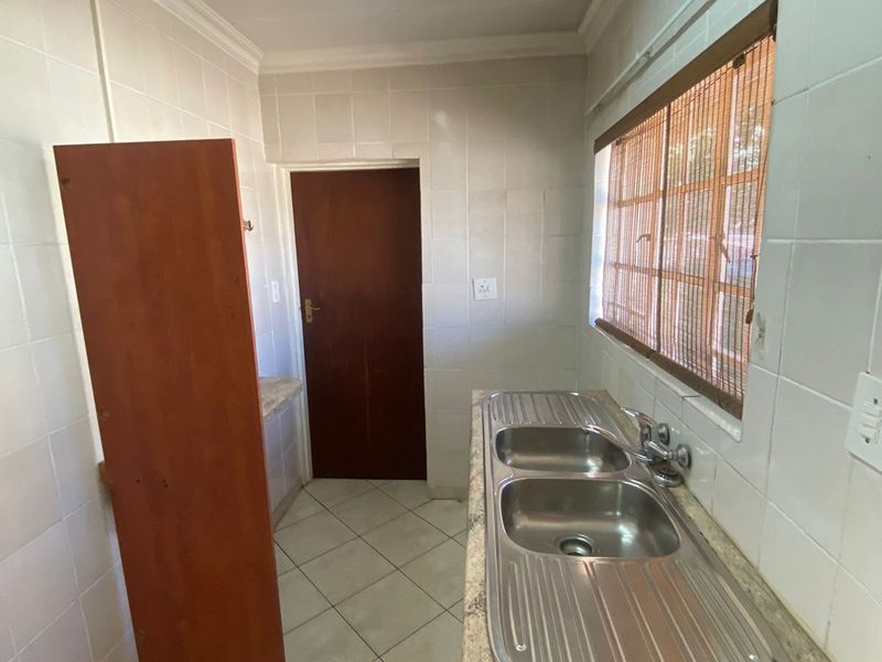 A functional scullery area featuring a double stainless steel sink, tiled walls, and tiled flooring, offering a practical space for kitchen preparation and wash-up.
