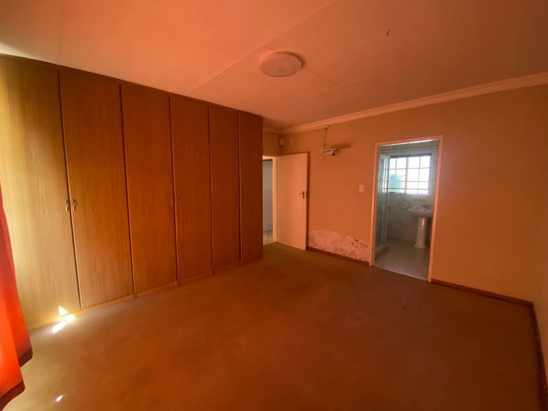 A bedroom featuring built-in wooden cupboards and an en-suite bathroom, showing signs of wall dampness and requiring cosmetic updates.