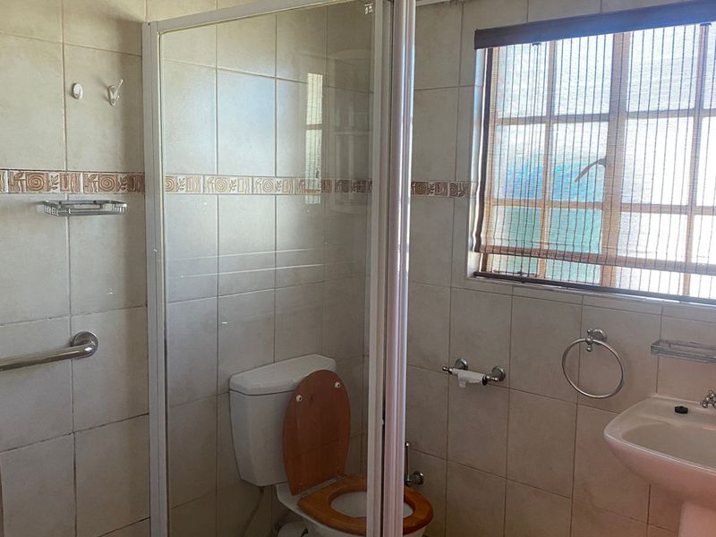 A functional bathroom featuring a shower enclosure, pedestal basin, and toilet with neutral wall and floor tiling.