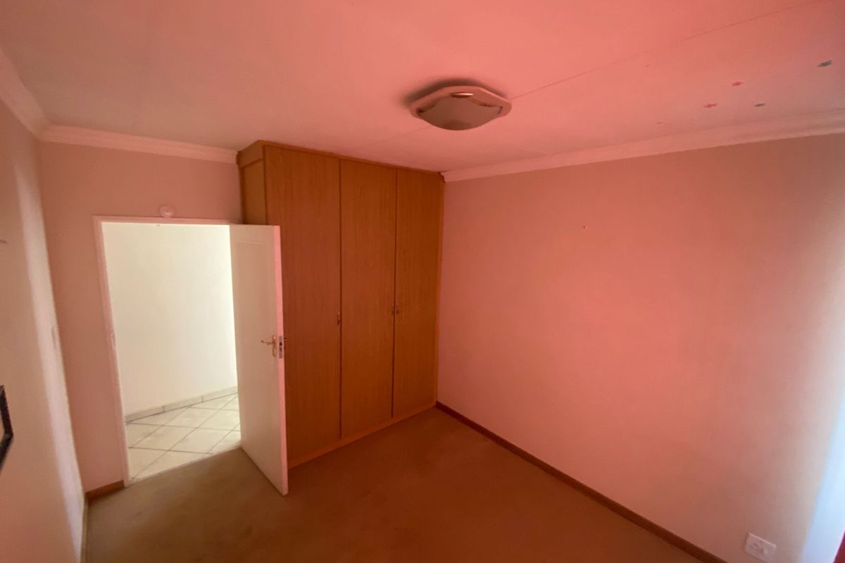A vacant bedroom featuring built-in wooden cupboards, neutral walls, and carpeted flooring, offering a blank canvas for personalization.
