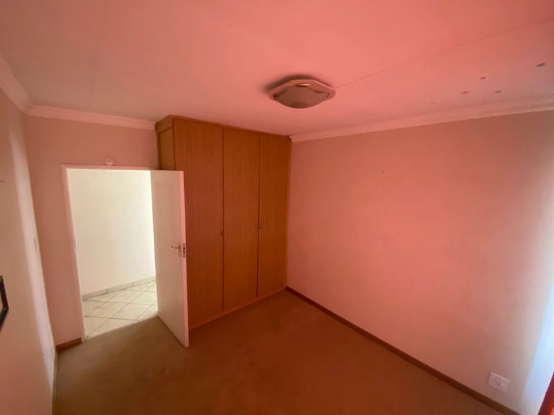 A vacant bedroom featuring built-in wooden cupboards, neutral walls, and carpeted flooring, offering a blank canvas for personalization.