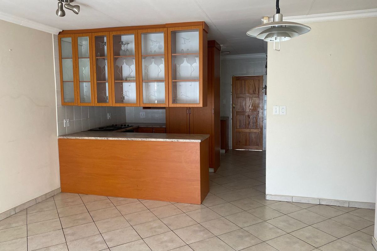 A functional kitchen area featuring built-in wooden cabinetry, a breakfast counter, tiled flooring, and a built-in hob, offering a blank canvas for modernization.