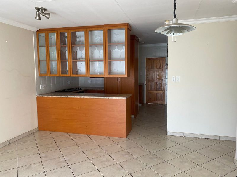 A functional kitchen area featuring built-in wooden cabinetry, a breakfast counter, tiled flooring, and a built-in hob, offering a blank canvas for modernization.