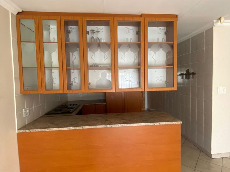 A functional kitchen area featuring built-in wooden cabinetry, glass-fronted display units, a laminate countertop, and a built-in electric hob with tiled finishes.