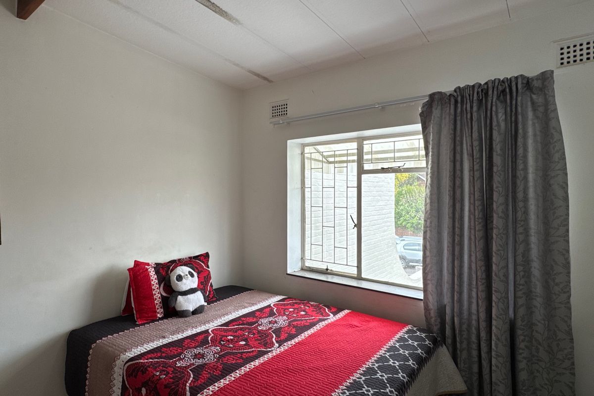 A bedroom featuring a window with security bars and visible ceiling damage requiring maintenance.