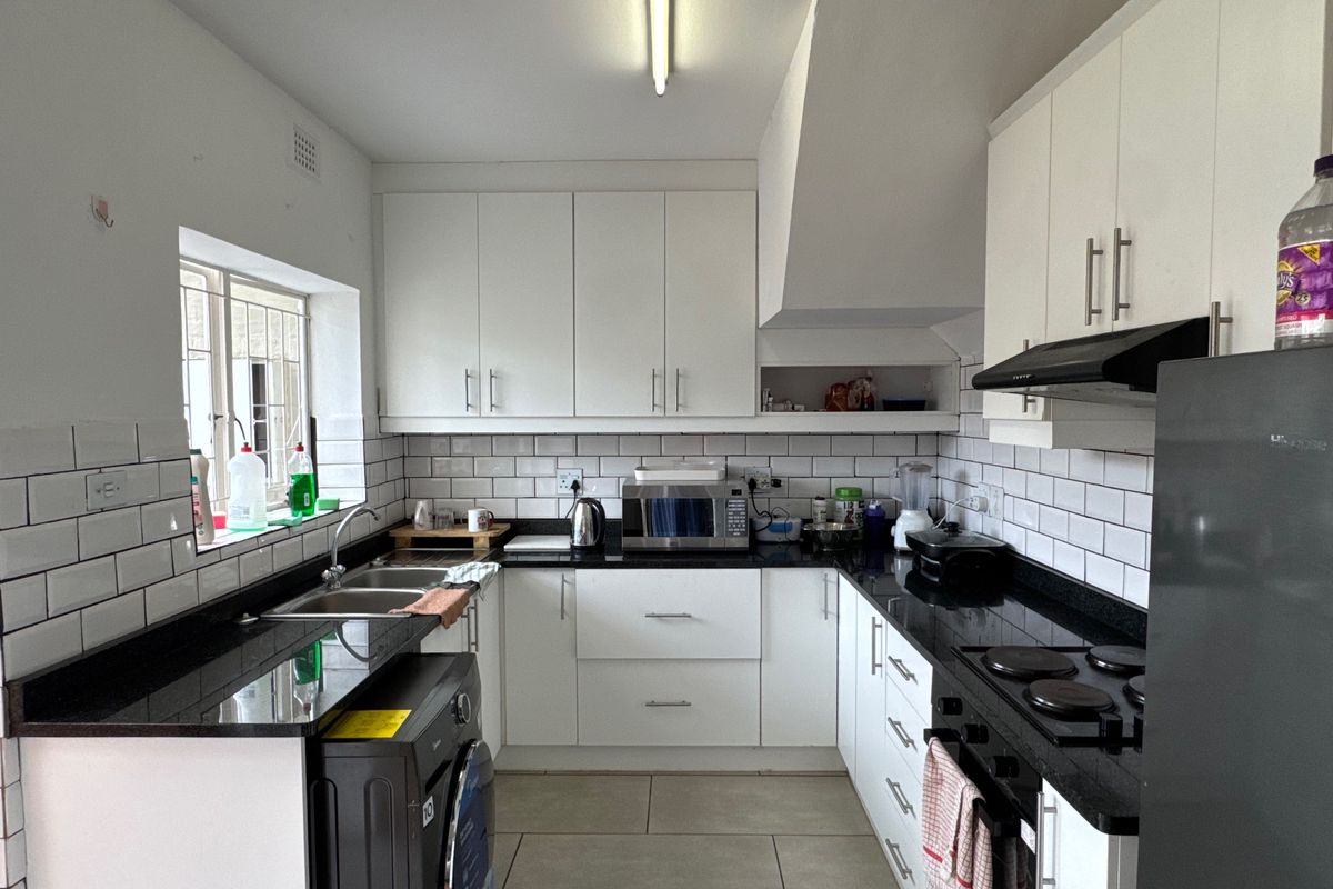 A functional kitchen featuring white cabinetry, black granite countertops, subway tile backsplash, and integrated electric hob with extractor fan.