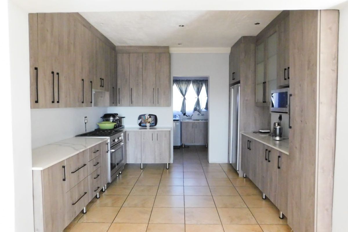 Modern galley-style kitchen featuring wood-grain cabinetry, stone countertops, integrated oven, and a tiled floor, with an adjacent scullery area visible.