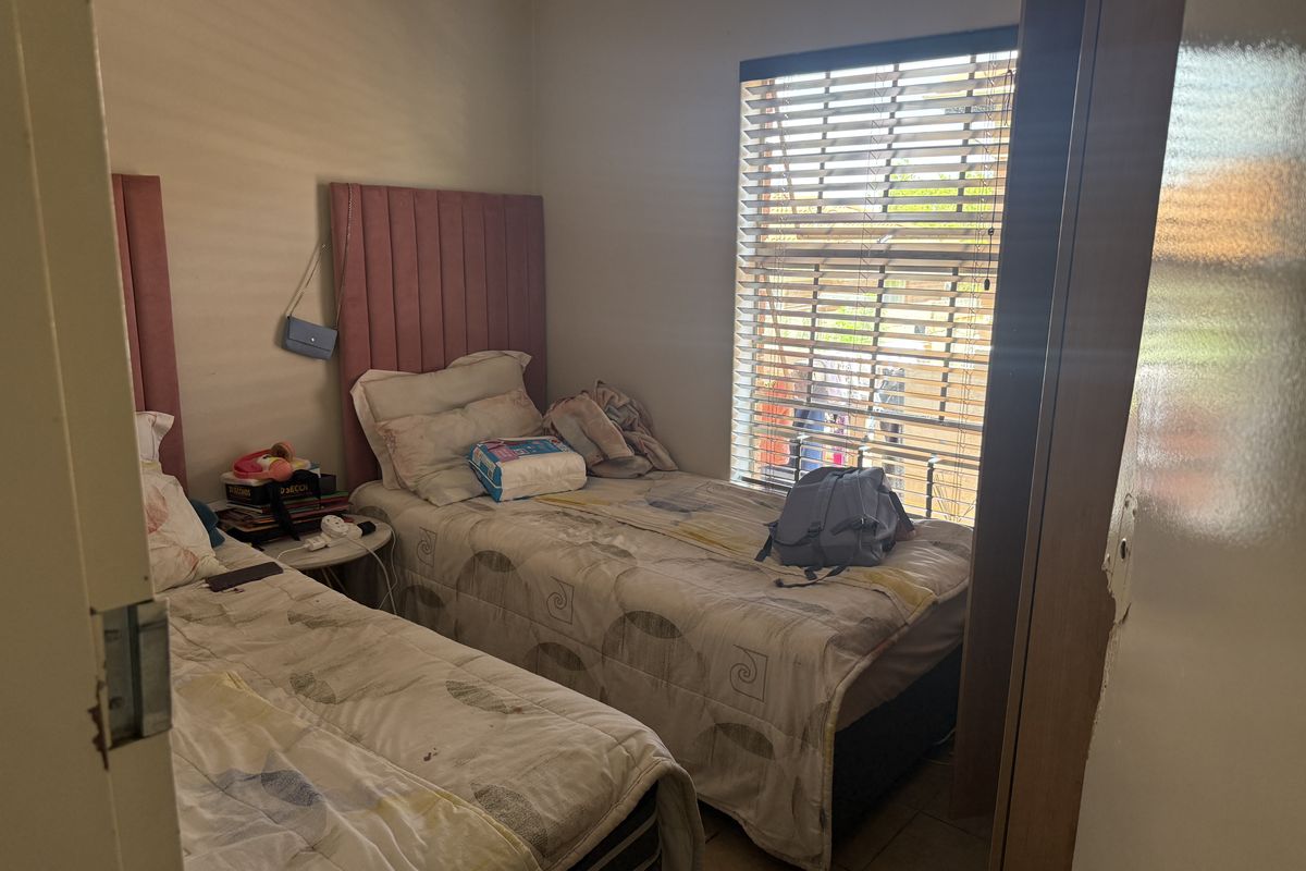 A bedroom featuring tiled flooring, a window with fitted blinds, and built-in headboards.