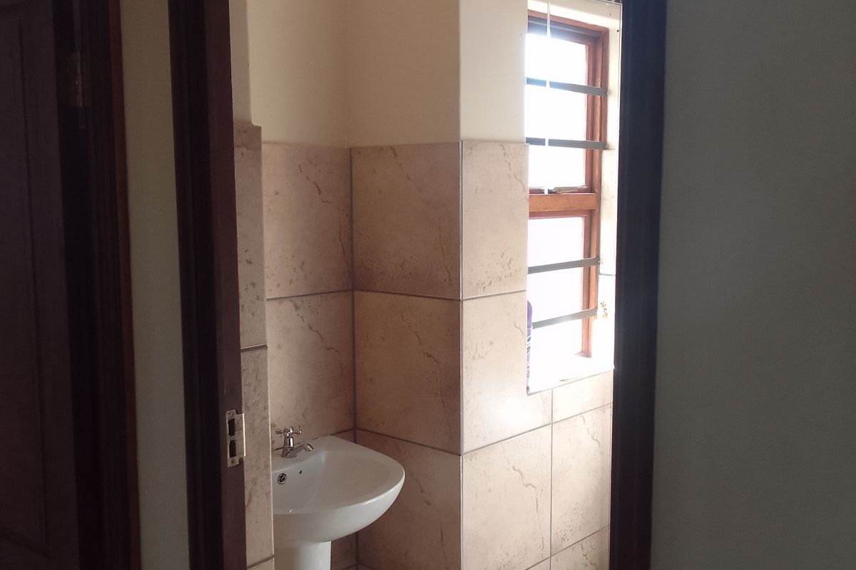 A compact bathroom featuring a pedestal basin, tiled walls, and a window providing natural light.