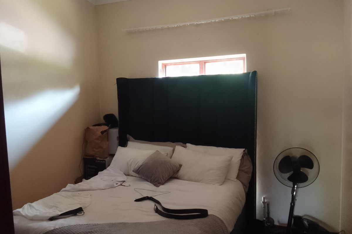 A bedroom featuring a high headboard, neutral wall finishes, and a small window providing natural light.