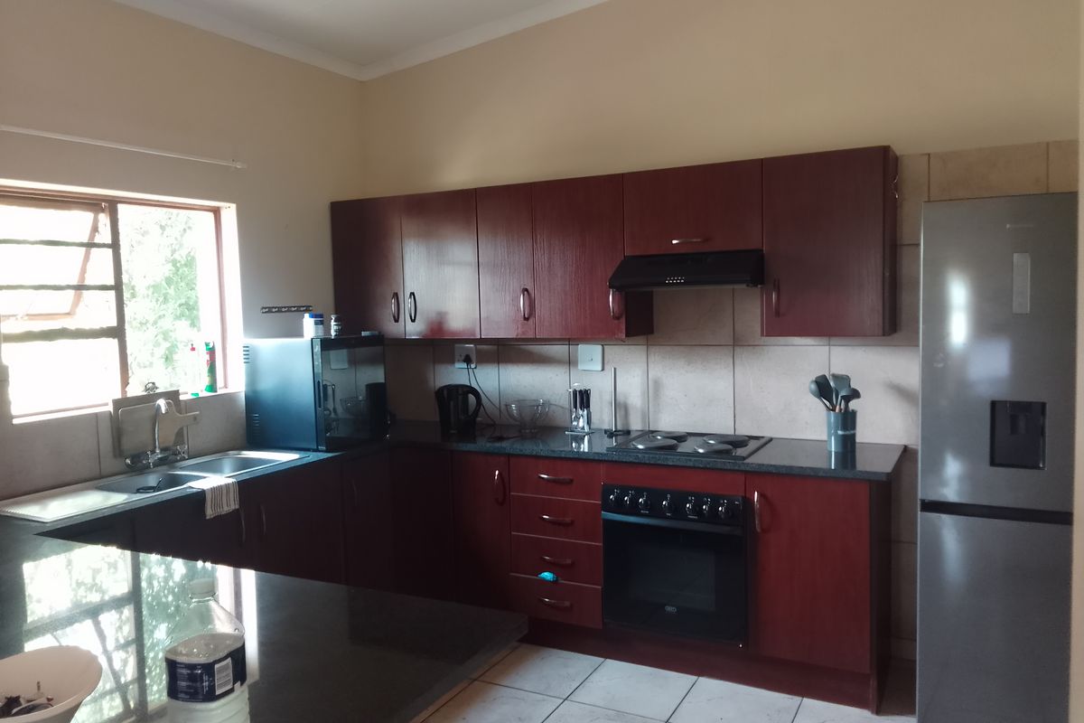 Functional kitchen featuring dark wood cabinetry, granite countertops, built-in oven, electric hob, extractor fan, and a double sink with tiled flooring.