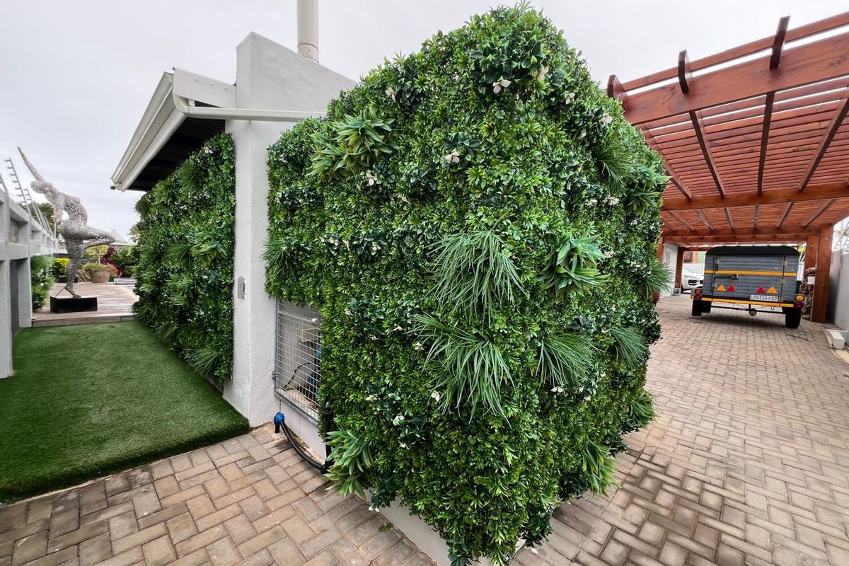 A well-maintained rear exterior area featuring a decorative artificial vertical garden wall, paved driveway, and a wooden pergola structure.