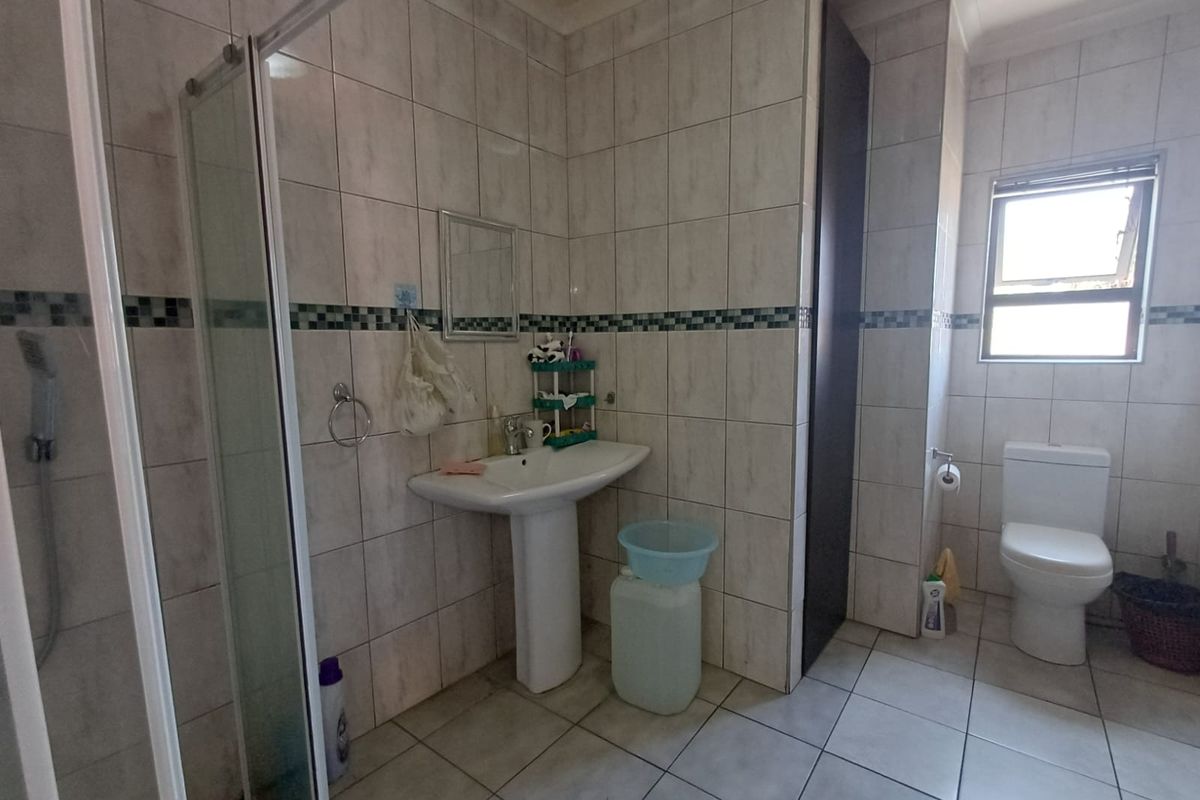 A functional bathroom featuring a pedestal basin, a glass-enclosed shower, and a standard toilet with neutral wall and floor tiling.