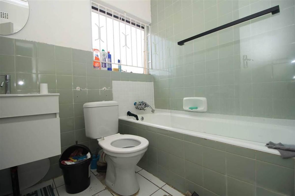 A dated bathroom featuring a bathtub with a glass screen, a wall-mounted vanity, and a toilet, finished with light green wall tiles.