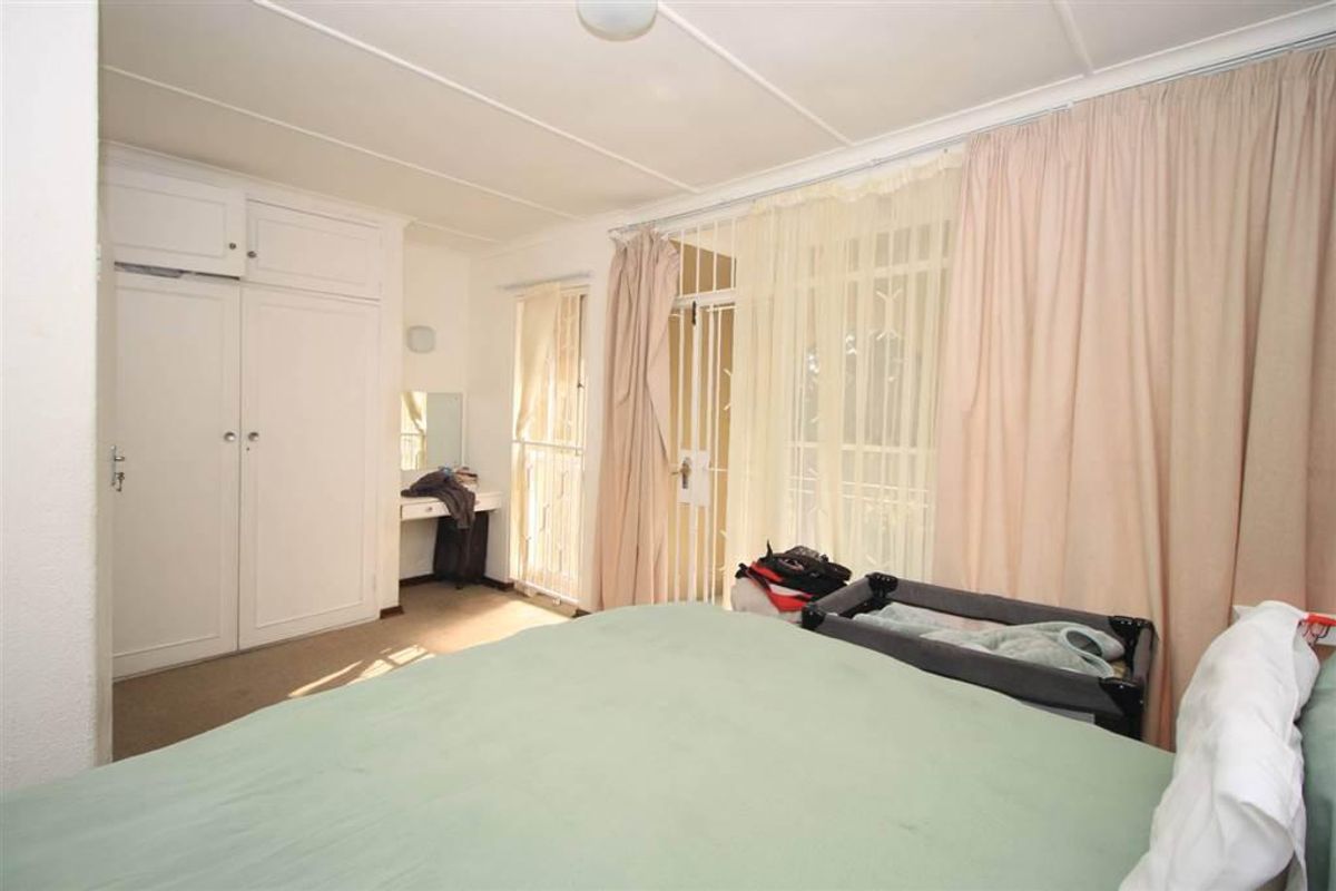 A bedroom featuring built-in wardrobes, carpeted flooring, and access to an outdoor area through a security gate.