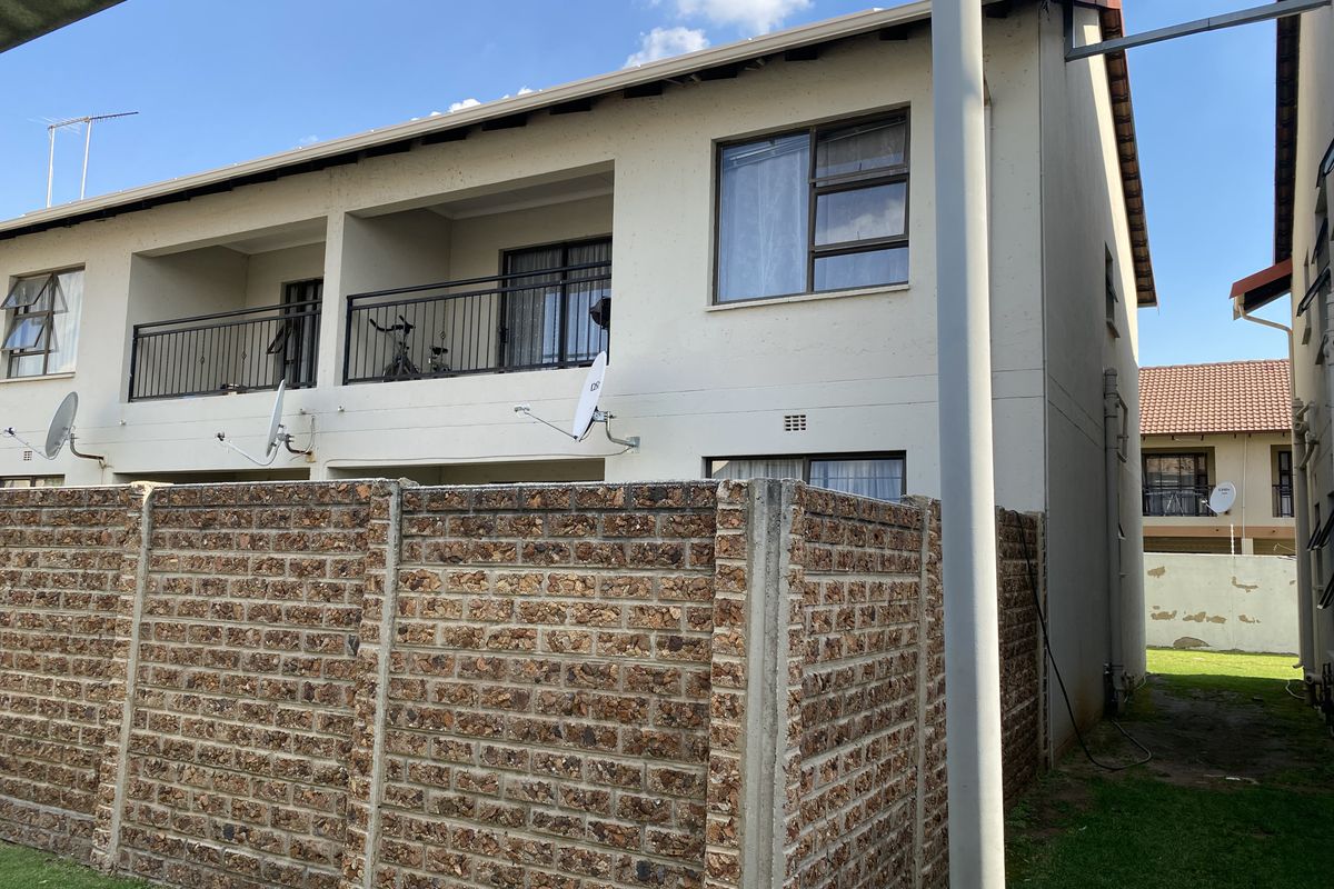 Rear view of a double-story townhouse featuring a private balcony with metal balustrades and a brick boundary wall enclosing the garden area.