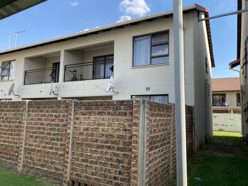Rear view of a double-story townhouse featuring a private balcony with metal balustrades and a brick boundary wall enclosing the garden area.
