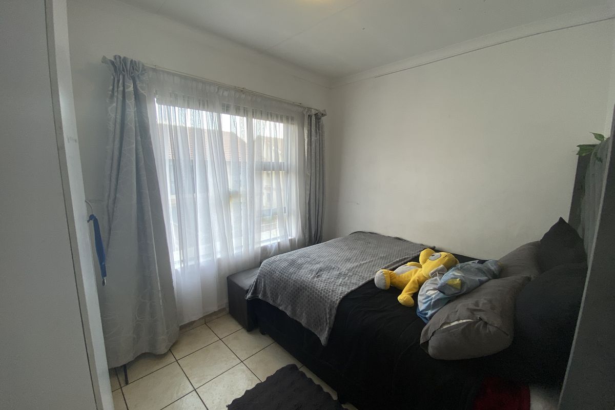 A compact bedroom featuring tiled flooring, a built-in cupboard, and a window with curtain treatments.