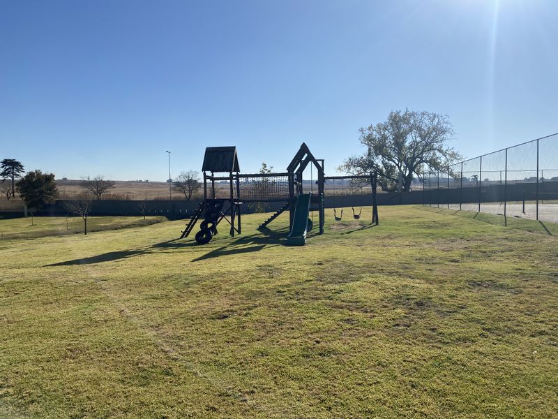 Outdoor communal recreational area featuring a playground set and perimeter fencing within a landscaped estate setting.