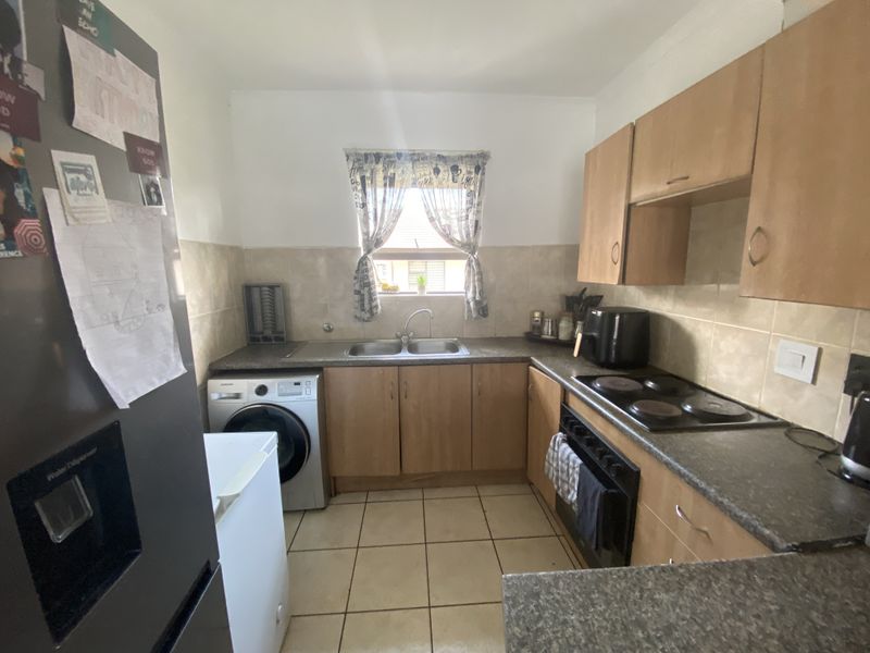 Functional kitchen featuring laminate cabinetry, double bowl sink, built-in electric oven, hob, and tiled splashback with integrated laundry plumbing.