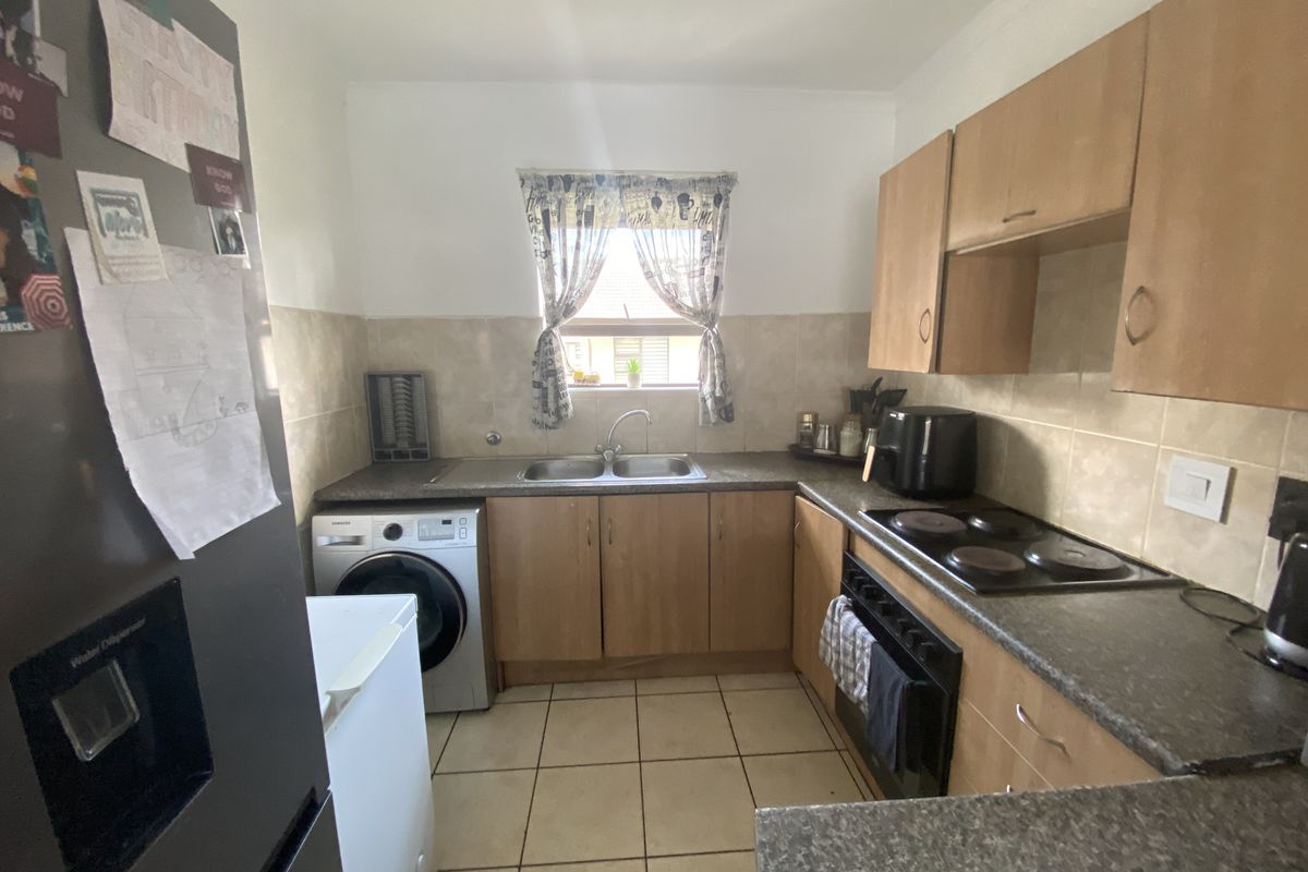 Functional kitchen featuring laminate cabinetry, double bowl sink, built-in electric oven, hob, and tiled splashback with integrated laundry plumbing.